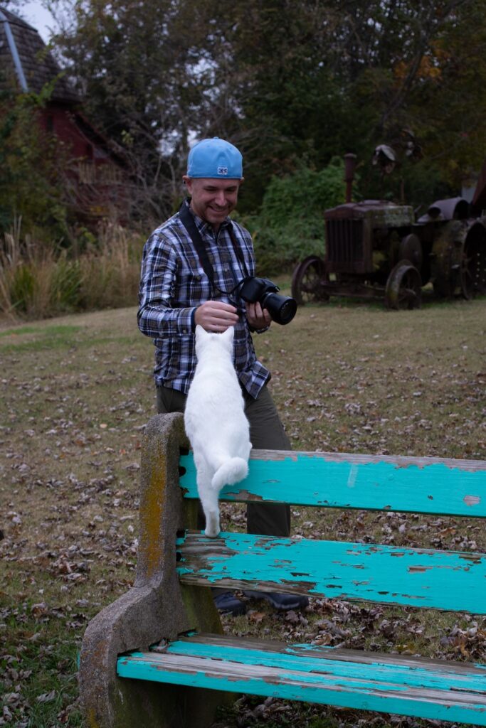 man in a backwards baseball cap petting a white cat