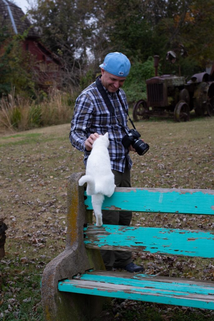 man in a backwards baseball cap petting a white cat