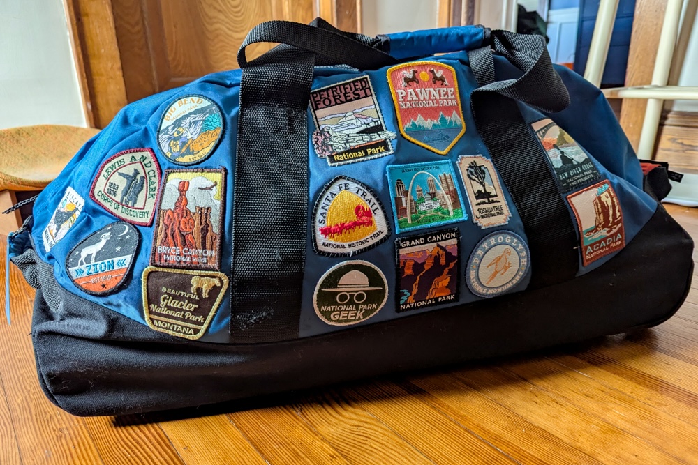 blue duffel bag covered in National Parks patches