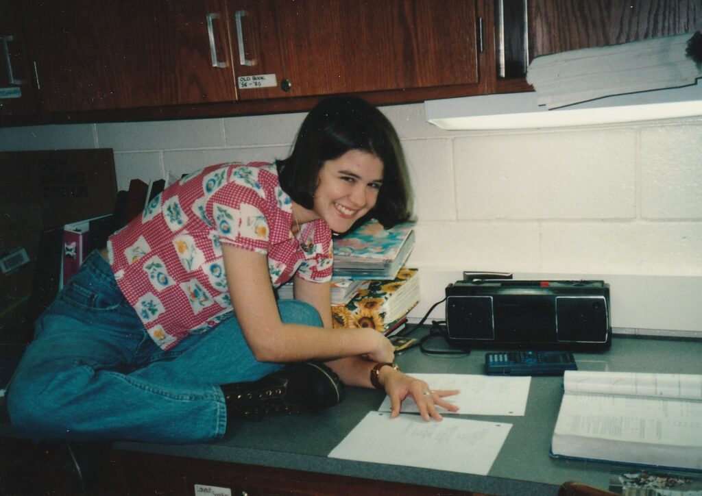 girl in pink shirt sitting on a counter in a schoolroom